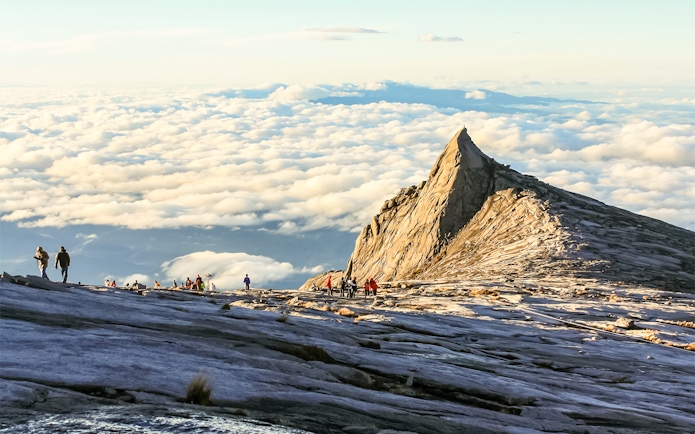 Hikers approaching the summit of Mount Kinabalu, surrounded by clouds.