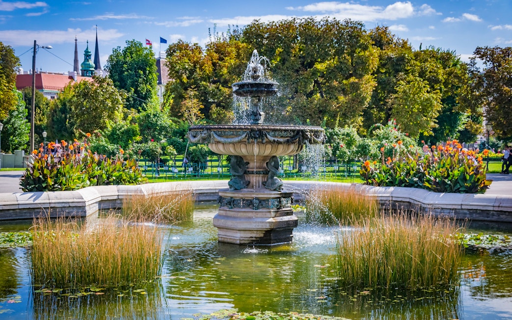 Fountain in the gardens of Hofburg Palace, Vienna, surrounded by lush greenery and flowers.