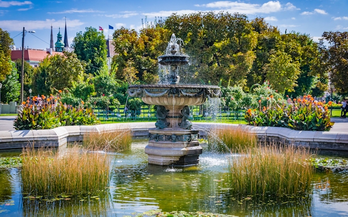 Fountain in the gardens of Hofburg Palace, Vienna, surrounded by lush greenery and flowers.