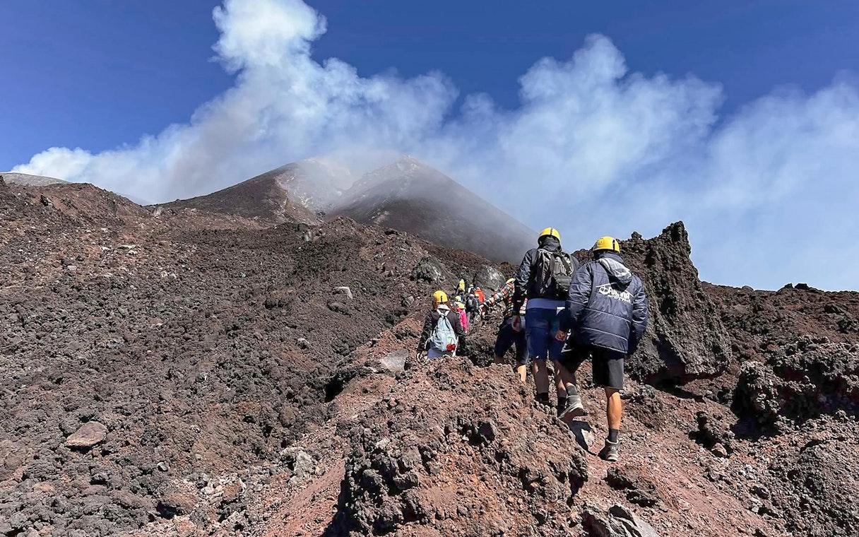 Hikers ascending rocky path towards Mount Etna summit, Sicily.