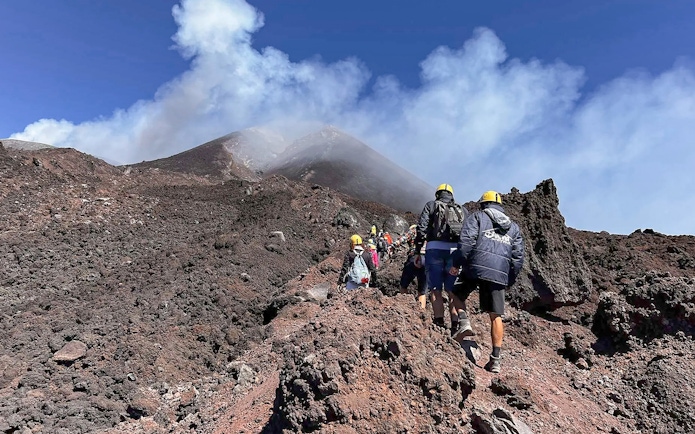Hikers ascending rocky path towards Mount Etna summit, Sicily.