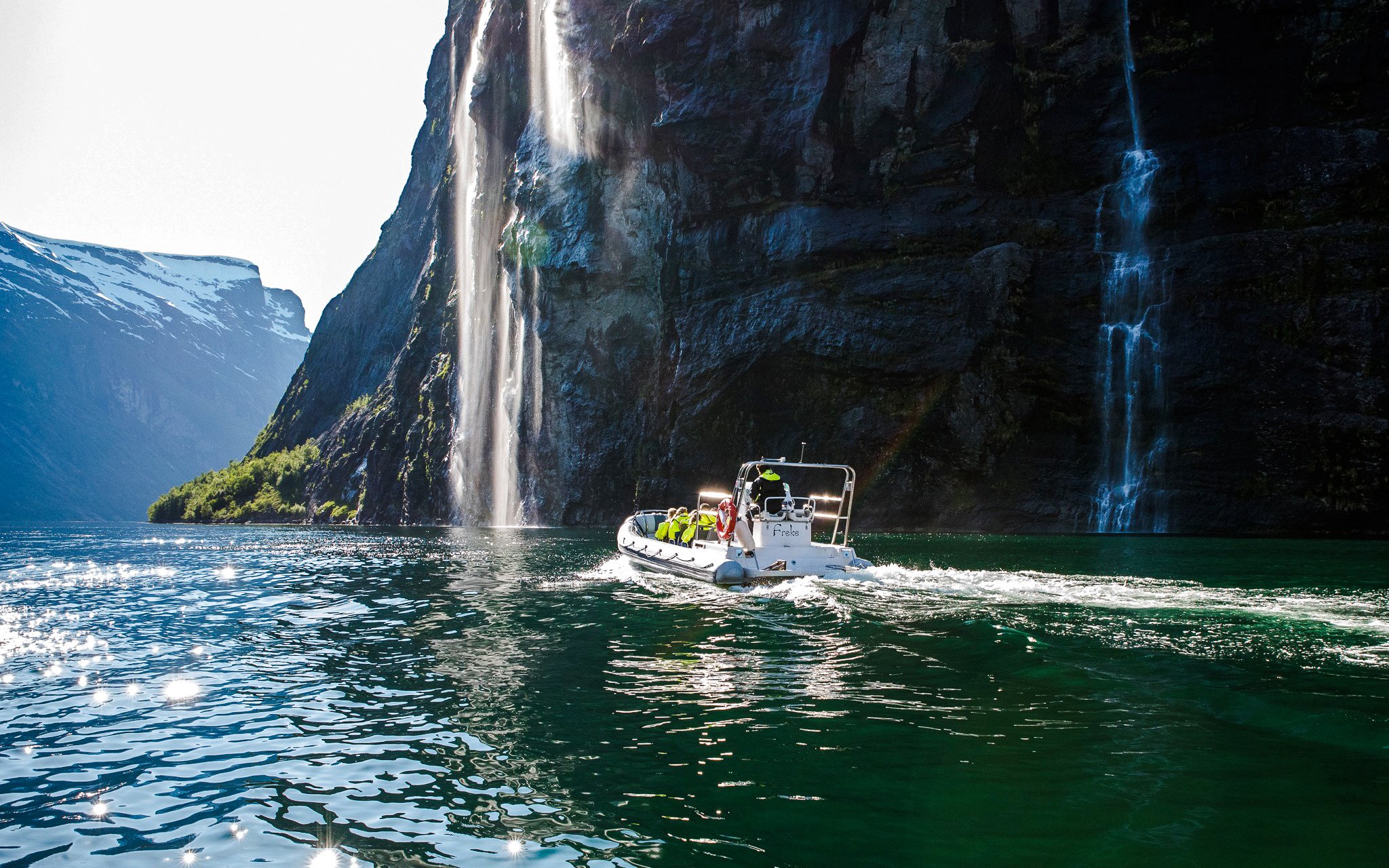 RIB boat on Geiranger Fjord near a waterfall, Norway.