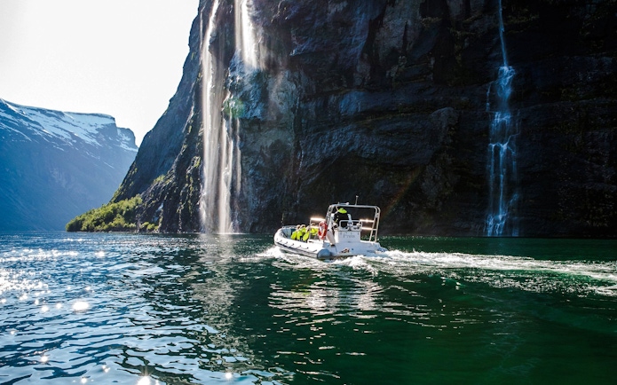 RIB boat on Geiranger Fjord near a waterfall, Norway.