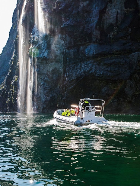 RIB boat on Geiranger Fjord near a waterfall, Norway.