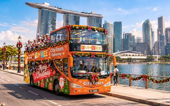 Open-top FunVee bus with Christmas decor on waterfront road, Marina Bay Sands in background, Singapore.
