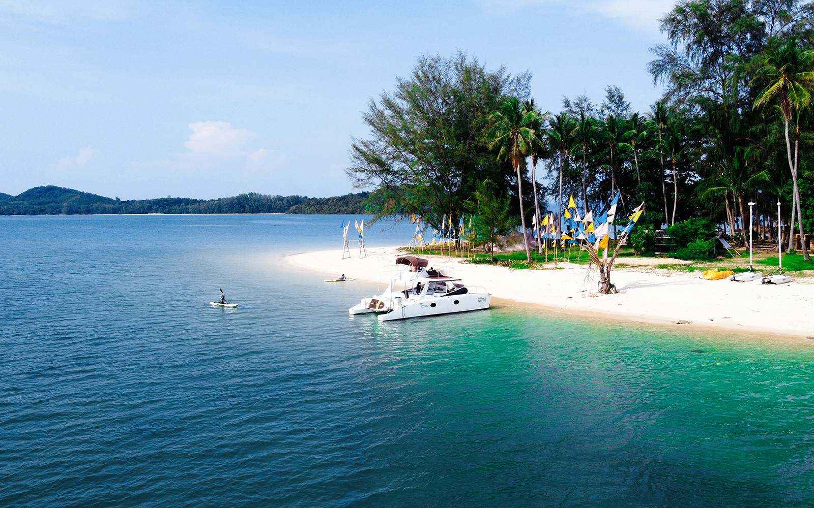 Catamaran anchored near Koh Naka Noi Beach, Phuket, with kayaker in turquoise water.