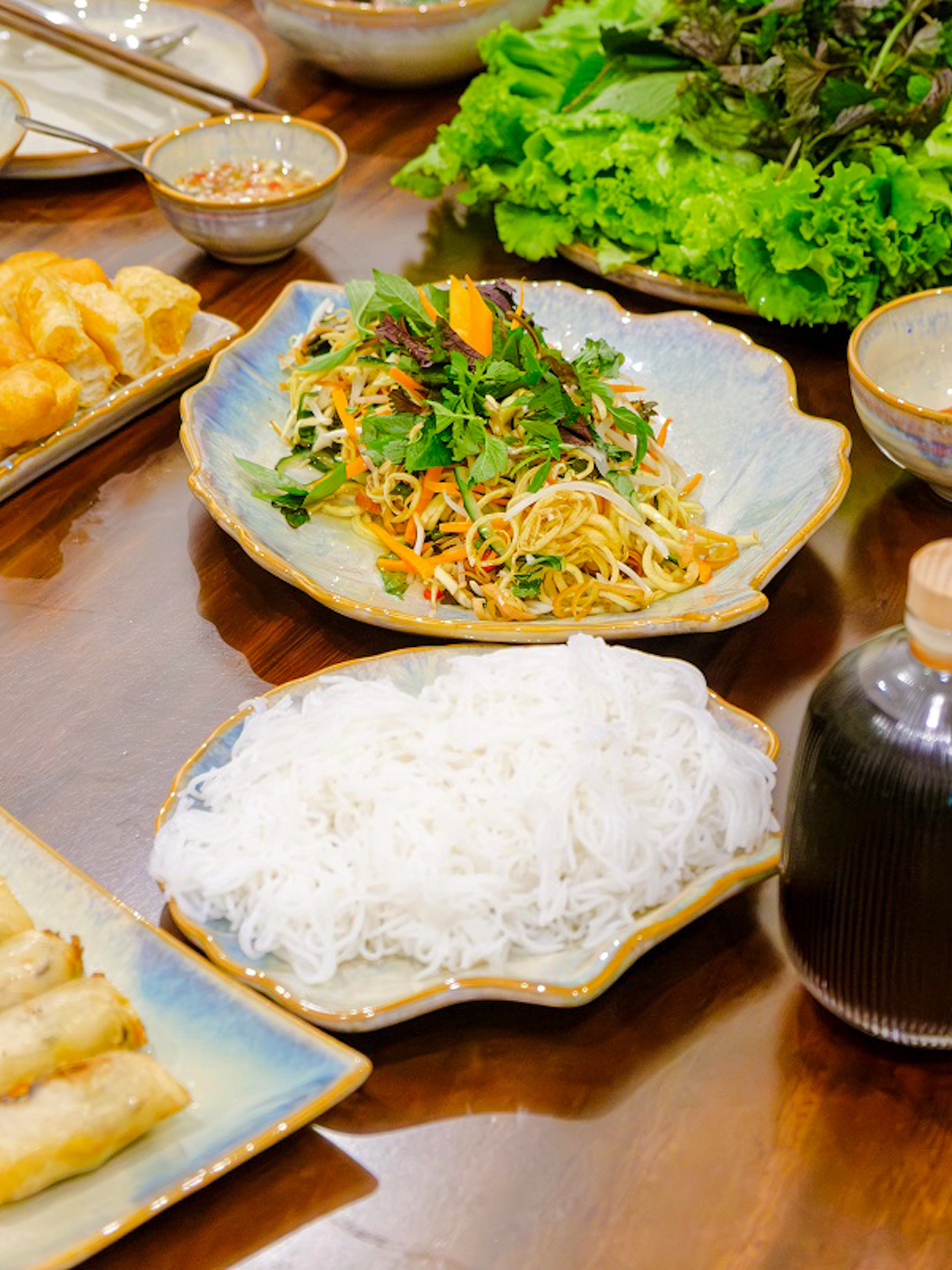 Traditional Vietnamese dishes with spring rolls, noodles, and herbs on a table in Hanoi cooking class.