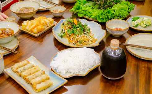 Traditional Vietnamese dishes with spring rolls, noodles, and herbs on a table in Hanoi cooking class.