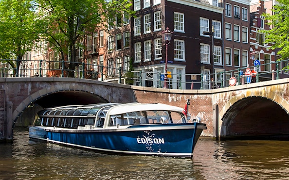 Canal boat cruising under a bridge in Amsterdam.