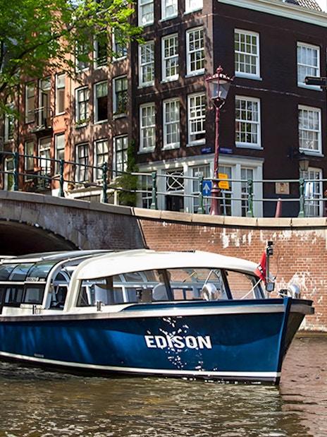 Canal boat cruising under a bridge in Amsterdam.