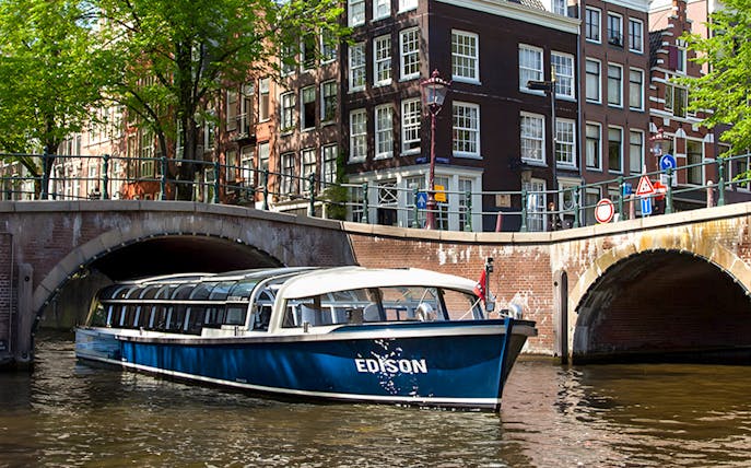 Canal boat cruising under a bridge in Amsterdam.