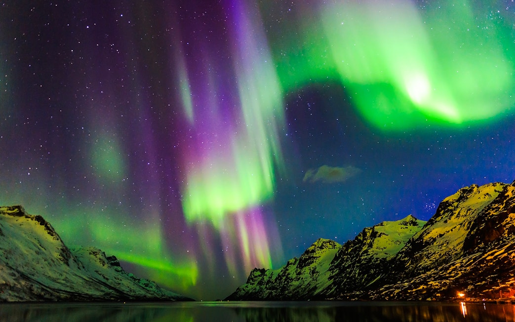 Northern Lights over snowy mountains viewed from a boat in Norway.