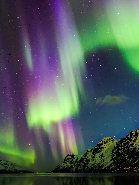 Northern Lights over snowy mountains viewed from a boat in Norway.