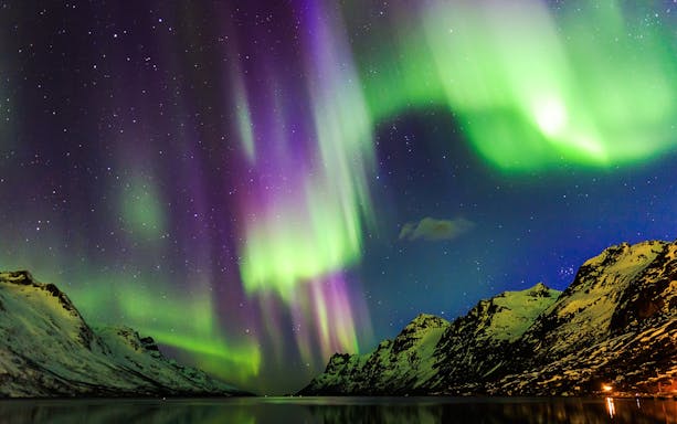 Northern Lights over snowy mountains viewed from a boat in Norway.