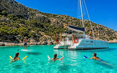 Catamaran cruise with people swimming and paddleboarding in clear waters near Rhodes.