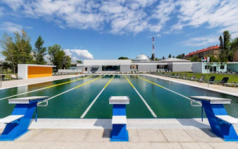 Outdoor pool at Pesterzsebet Bath, Budapest with diving boards and lounge chairs.