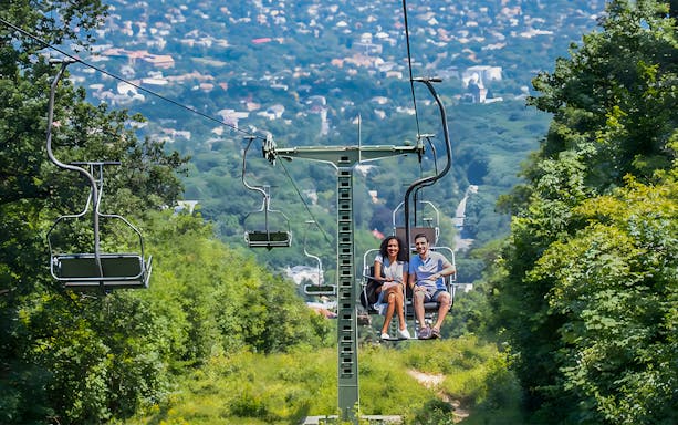 Gondola lift with passengers overlooking Budapest cityscape.