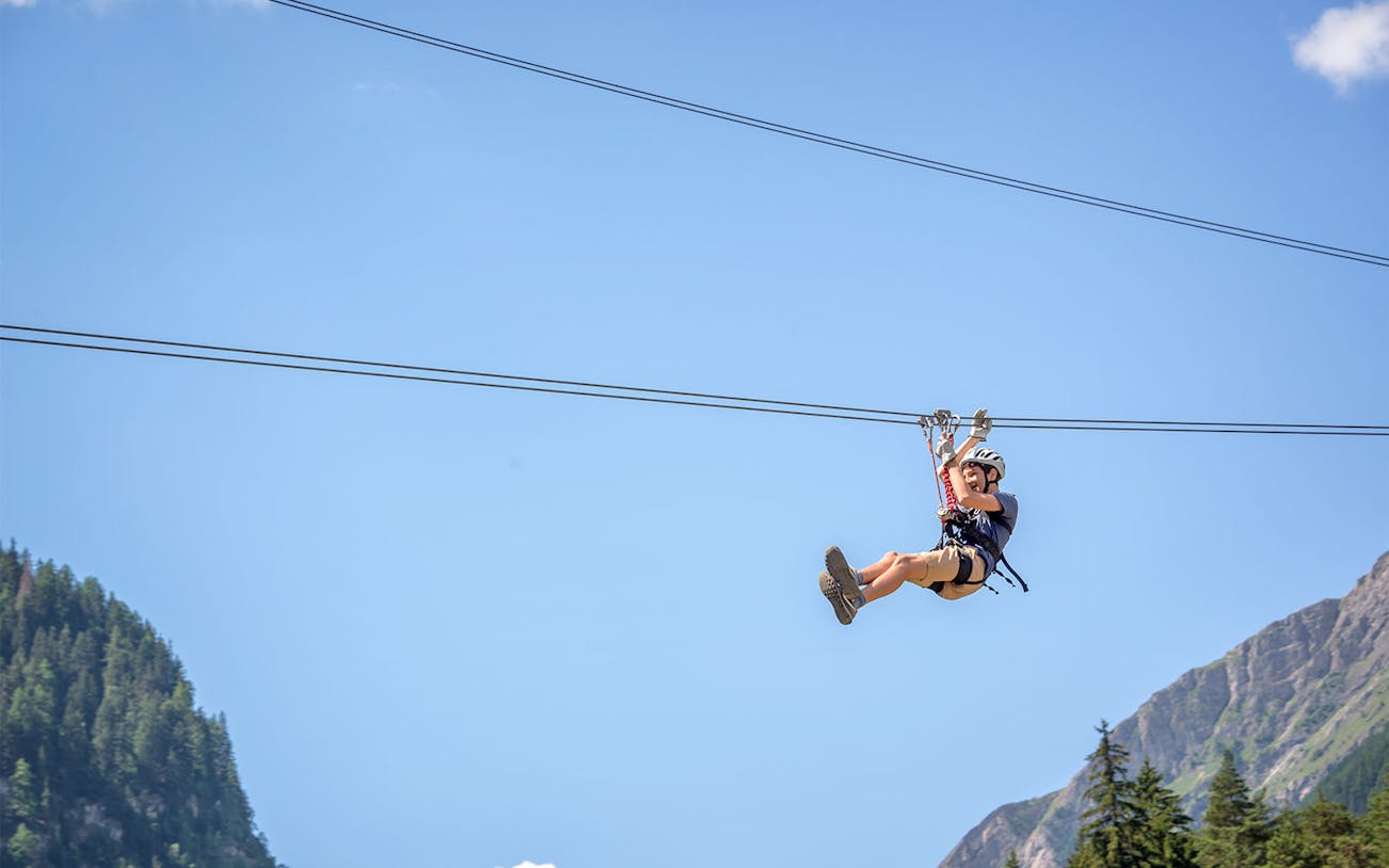 Person ziplining at Jebel Jais with mountain and forest backdrop.