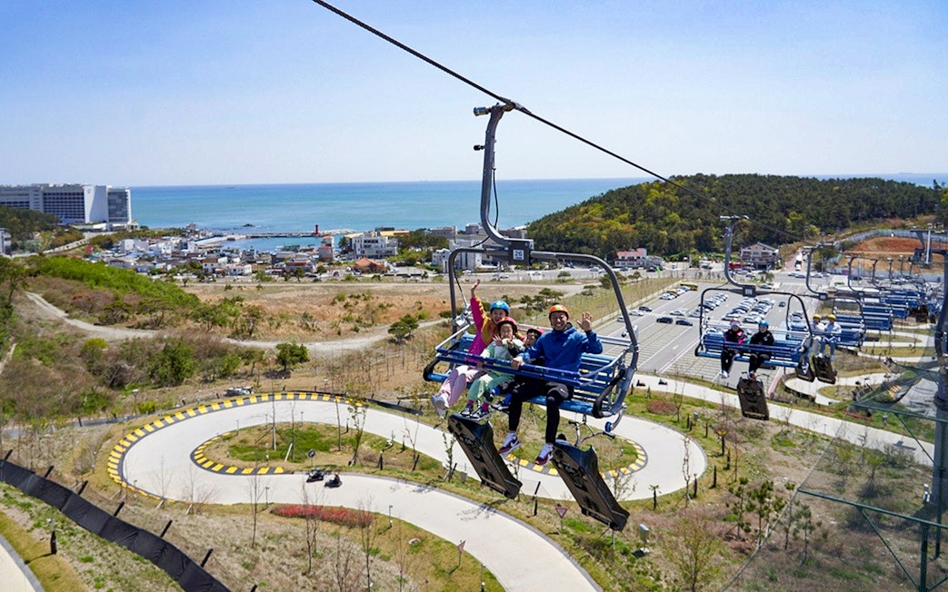 Family on chairlift at Skyline Luge Busan with coastal view in background.