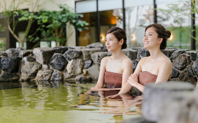 Friends enjoying a soak at Solaniwa Onsen, surrounded by natural stone and greenery.