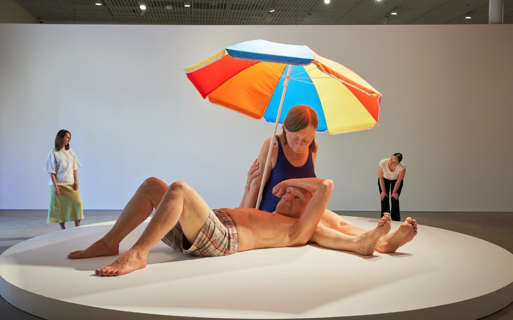 Couple under a colorful umbrella sculpture by Ron Mueck at Art Gallery of New South Wales, Sydney.