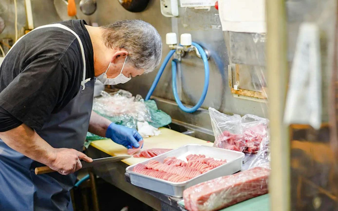 Chef slicing fish in Tsukiji Fish Market kitchen, Tokyo.