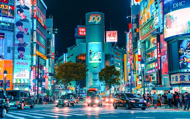 Shibuya Crossing at night with neon lights and traffic, Tokyo, Japan.