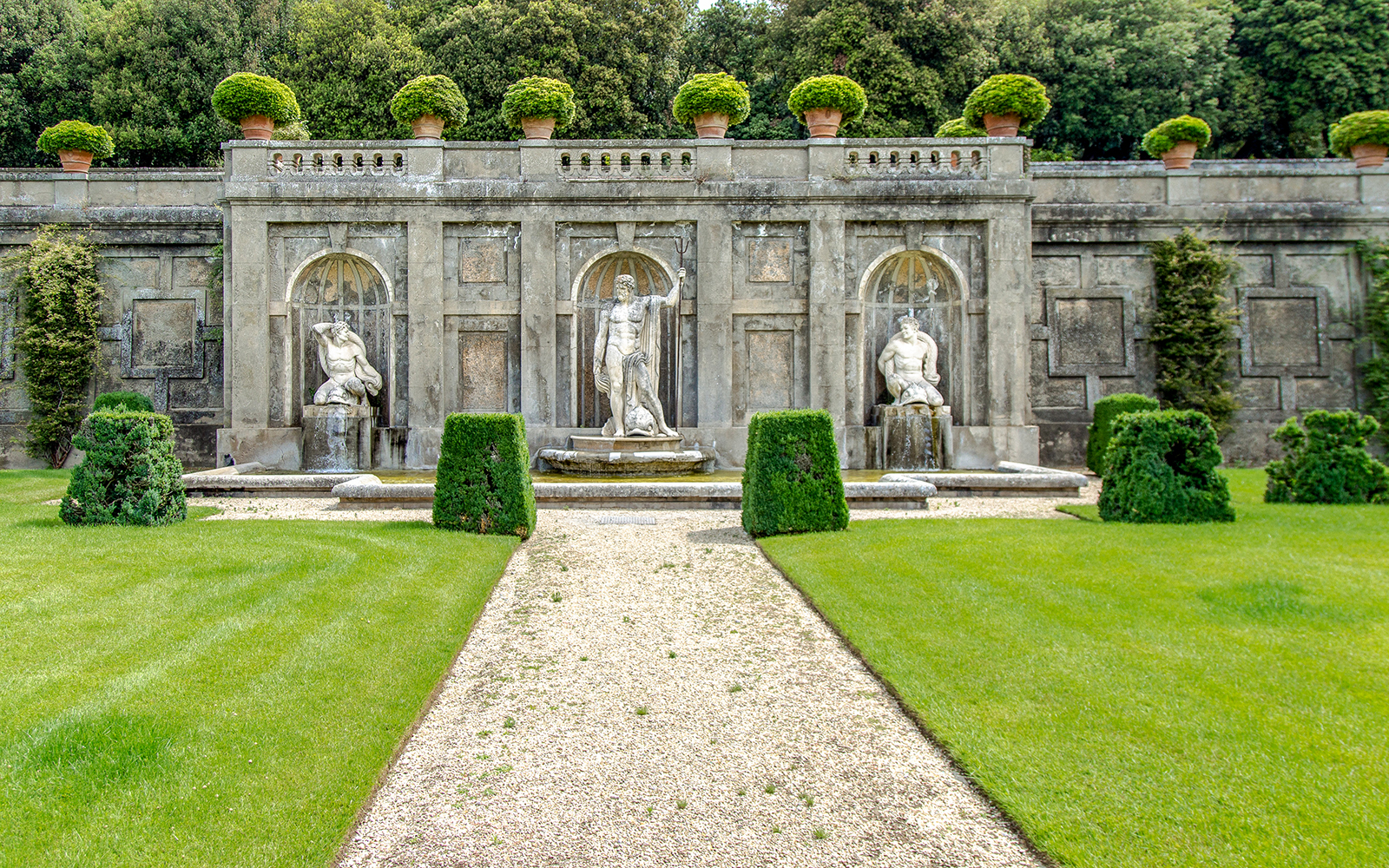 Sculptures in Pontifical Villa Gardens with manicured hedges and stone wall backdrop.