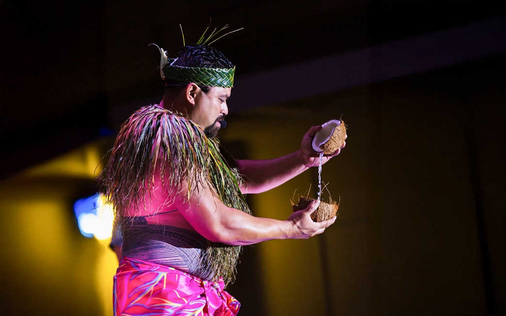 Performer at Moana Luau in Hawaii pouring coconut water during traditional Hawaiian ceremony.