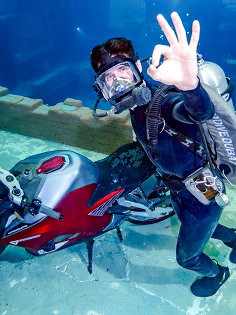Diver exploring underwater city ruins with a motorcycle, Sunken City Walk.