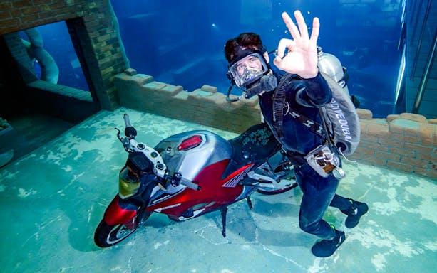 Diver exploring underwater city ruins with a motorcycle, Sunken City Walk.