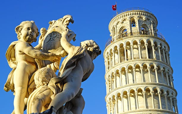 Statue of cherubs near the Leaning Tower of Pisa under a clear blue sky.