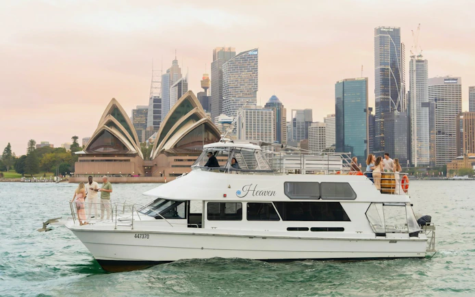 Sydney Harbour cruise boat with people enjoying drinks, Opera House and skyline in background.
