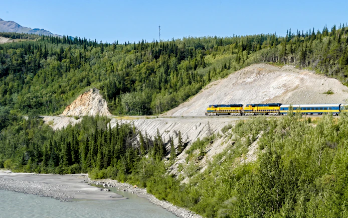 Alaska Railroad train traveling through forested mountains.