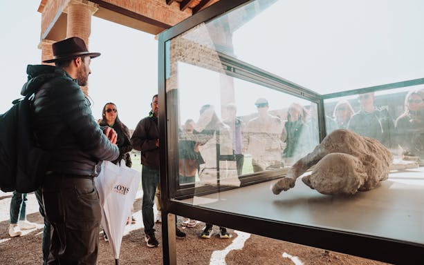 Tour group viewing a plaster cast of a victim in Pompeii's archaeological ruins.