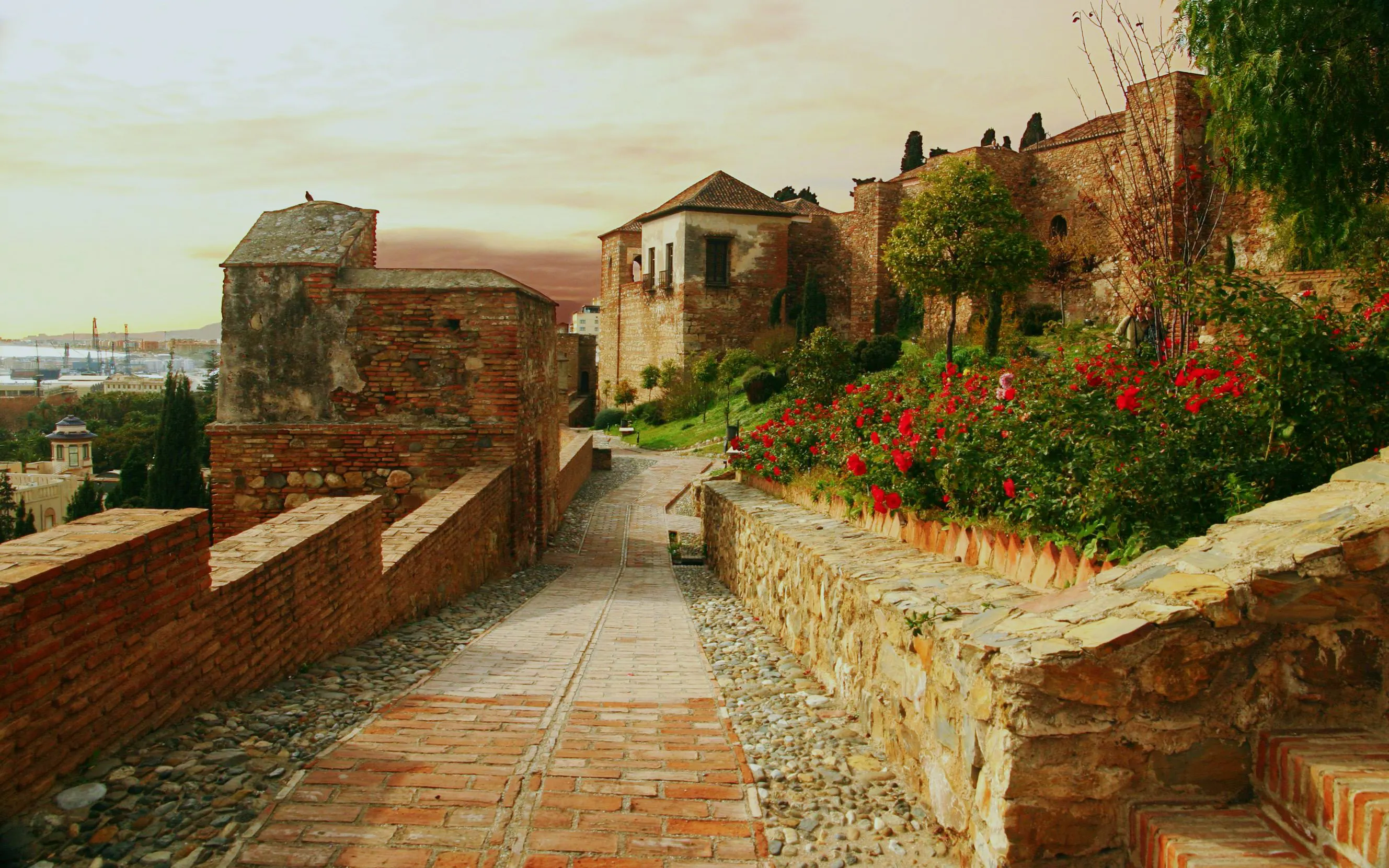 Gibralfaro Castle pathway with stone walls and red flowers in Málaga, Spain.