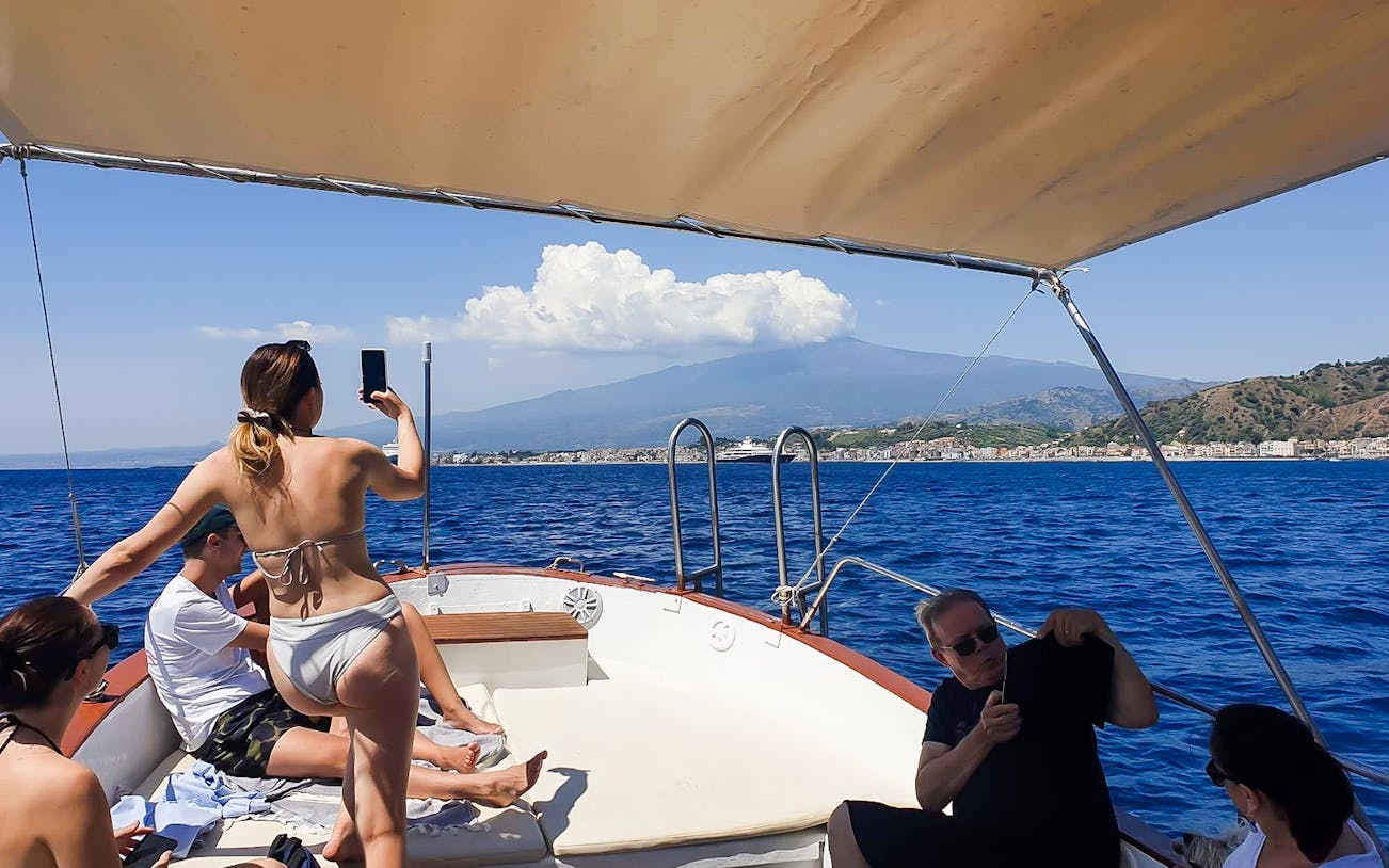 Excursion boat with tourists near Giardini Naxos, view of Taormina and Isola Bella in background.