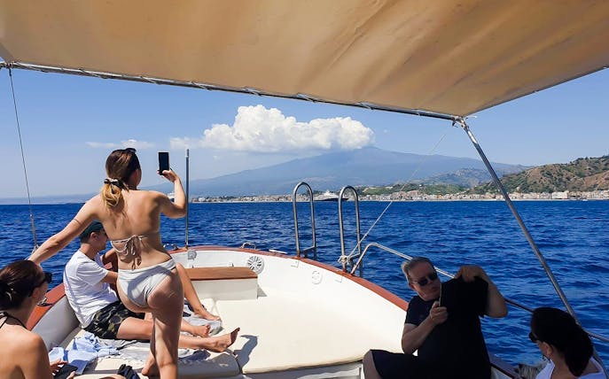 Excursion boat with tourists near Giardini Naxos, view of Taormina and Isola Bella in background.
