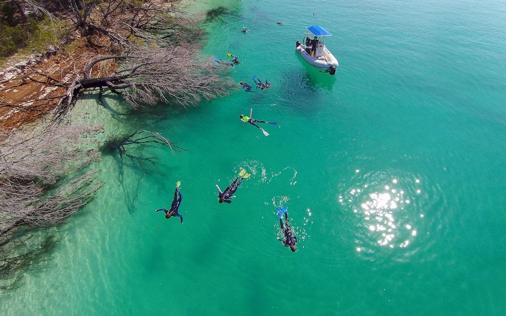 Snorkelers exploring clear waters near a boat on K'gari (Fraser Island) tour.