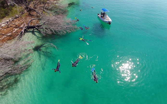 Snorkelers exploring clear waters near a boat on K'gari (Fraser Island) tour.