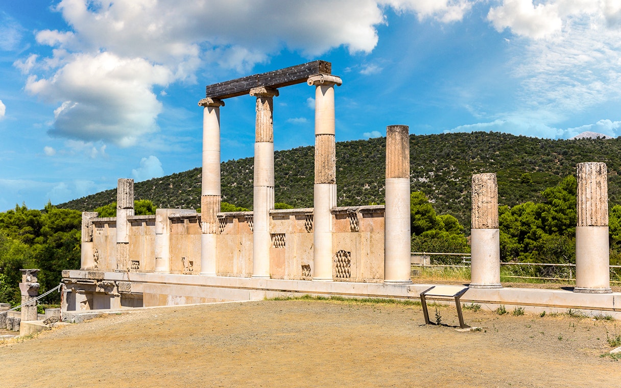 Ancient columns at Epidaurus Theatre, Greece, with scenic hillside backdrop.