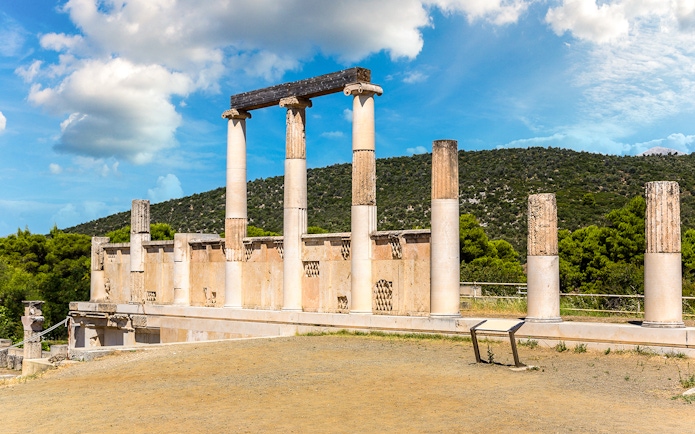 Ancient columns at Epidaurus Theatre, Greece, with scenic hillside backdrop.