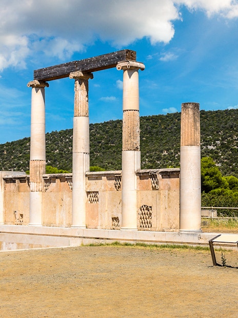 Ancient columns at Epidaurus Theatre, Greece, with scenic hillside backdrop.