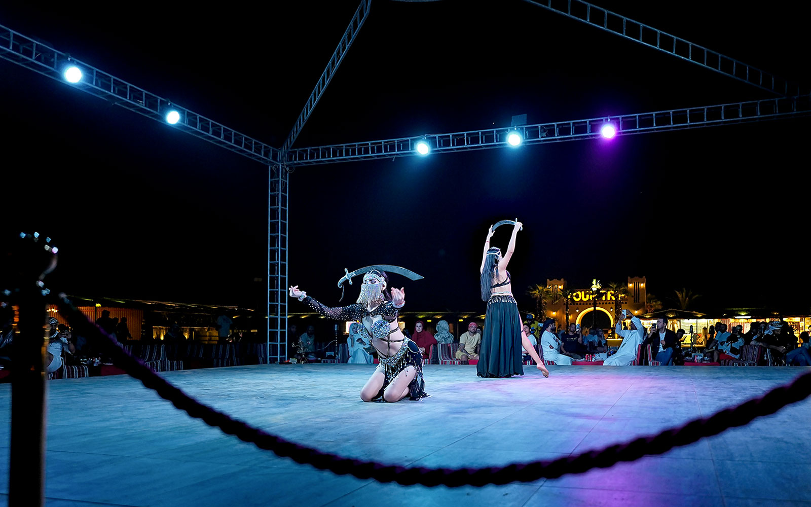 Evening desert safari performance with dancers on stage, audience watching.