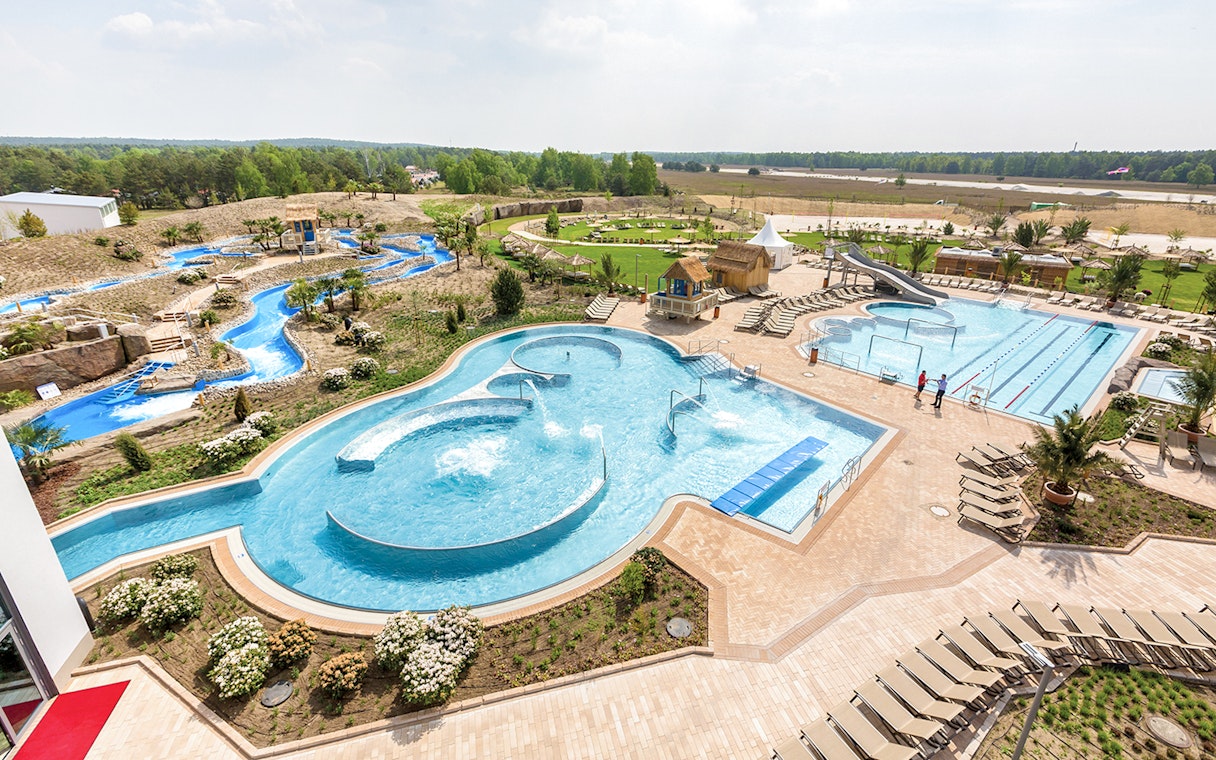 Outdoor pools and lazy river at Tropical Islands Resort, surrounded by greenery and lounge chairs.