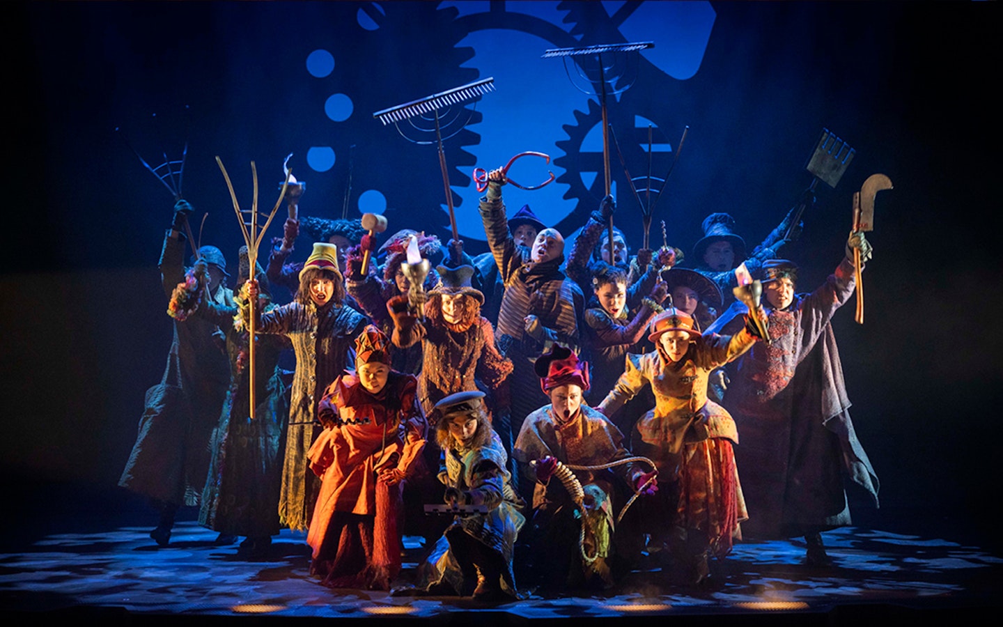 Performers on stage in a scene from the musical Wicked, holding farming tools.