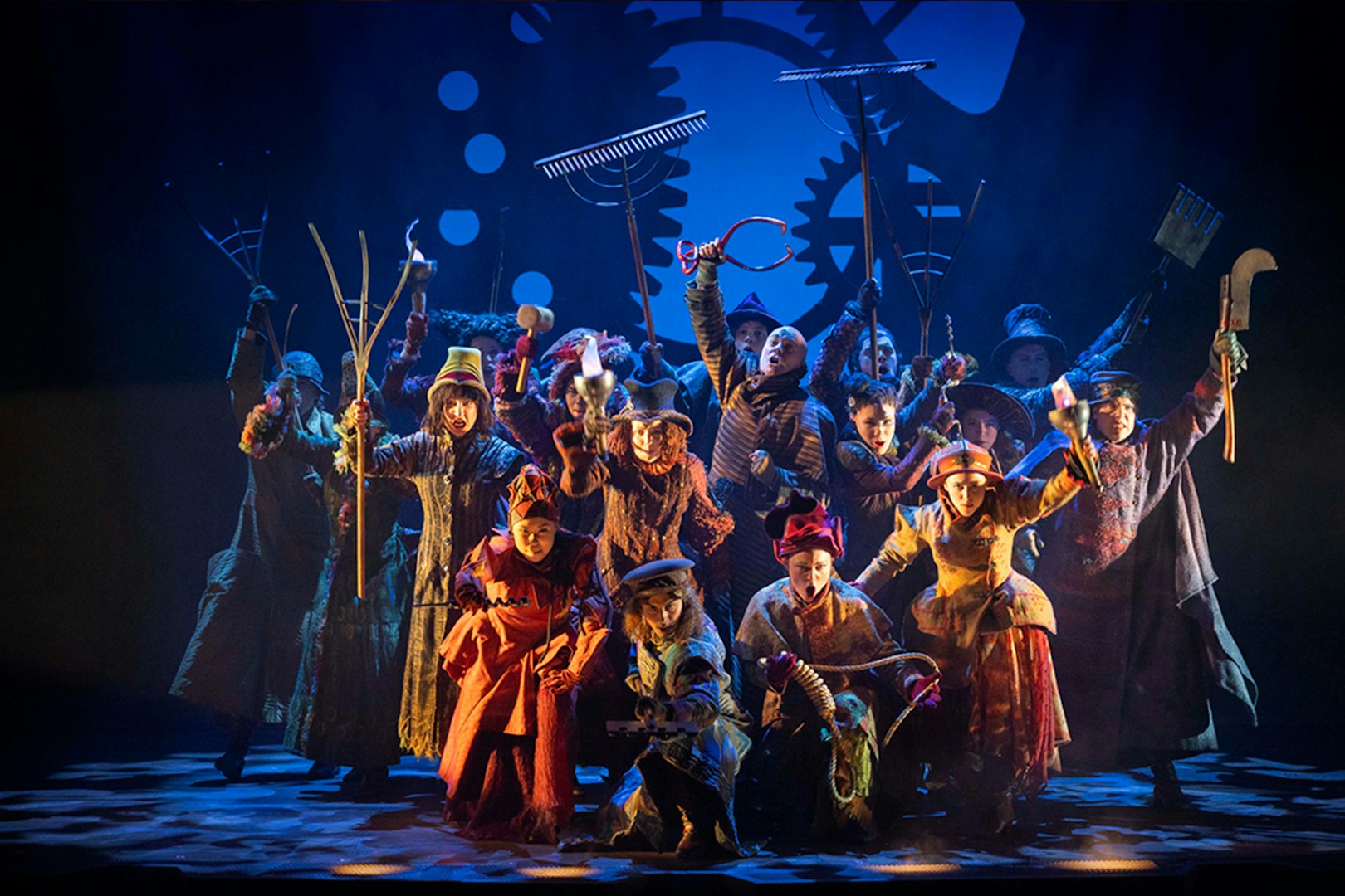 Performers on stage in a scene from the musical Wicked, holding farming tools.