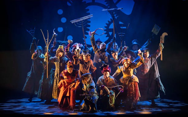 Performers on stage in a scene from the musical Wicked, holding farming tools.