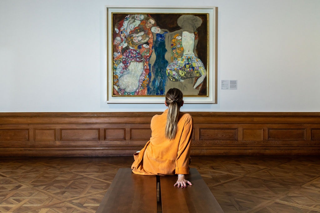 Visitor admiring Gustav Klimt painting at Belvedere Palace, Vienna.