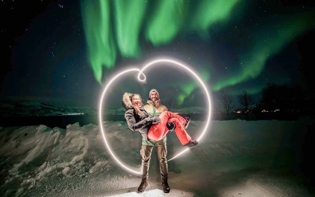 Guests under Northern Lights on Tromsø tour, surrounded by snow and light art.